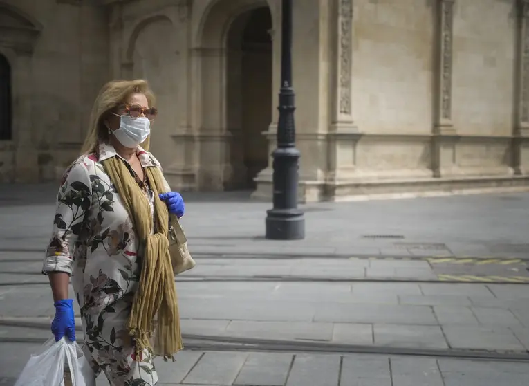 Una mujer camina con mascarilla y guantes.