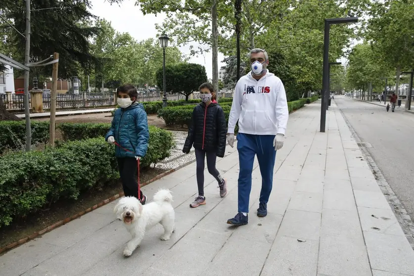 Dos ni&ntilde;os pasean con mascarillas, un adulto y un perro.