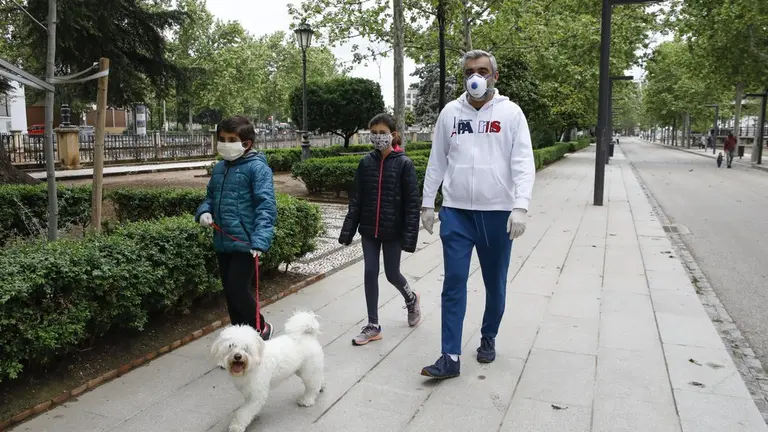 Dos ni&ntilde;os pasean con mascarillas, un adulto y un perro.